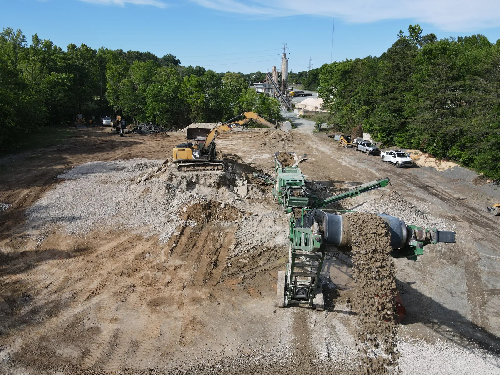 Excavator feeding waste concrete into a mobile crusher producing recycled aggregate